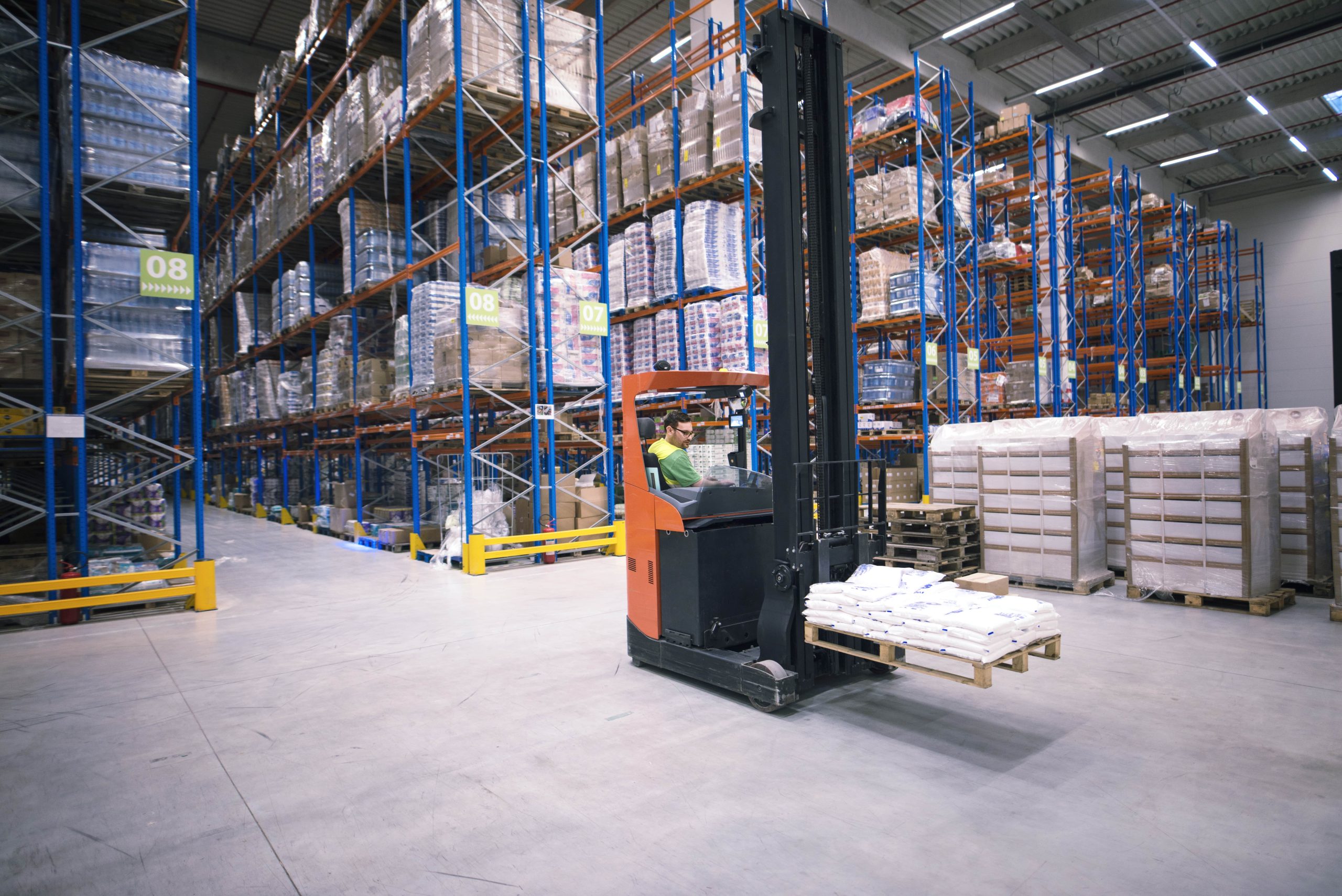 worker-operating-forklift-machine-relocating-goods-large-warehouse-center-min